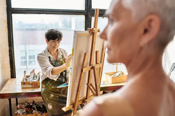 Skilled female artist painting portrait on blurred mature model in craft workshop, inspiration — Stock Photo
