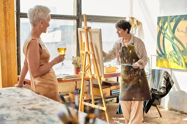 Abile artista donna pittura elegante modello in posa con bicchiere di vino in studio d'arte, processo artistico — Foto stock