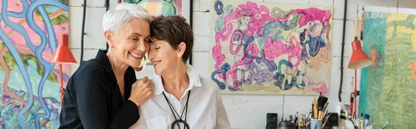 Joyeuses et branchées artistes lesbiennes souriant les yeux fermés dans un studio d'art, bannière horizontale — Photo de stock