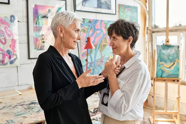Vue latérale de couple lesbien heureux et élégant d'artistes parlant dans l'atelier d'art moderne, travail d'équipe — Photo de stock