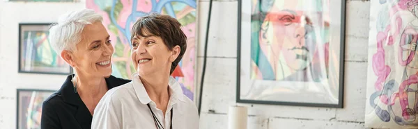 Glücklich reife lesbische Künstler, die einander in der Werkstatt für moderne Kunst umarmen und anschauen, Banner — Stockfoto