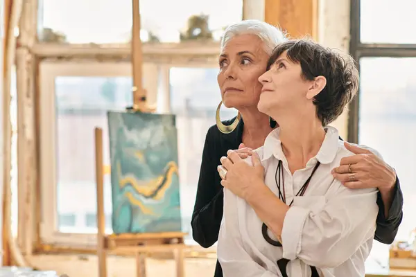Artistes lesbiennes coûteux et à la mode regardant loin dans le studio d'art moderne avec des peintures créatives — Photo de stock