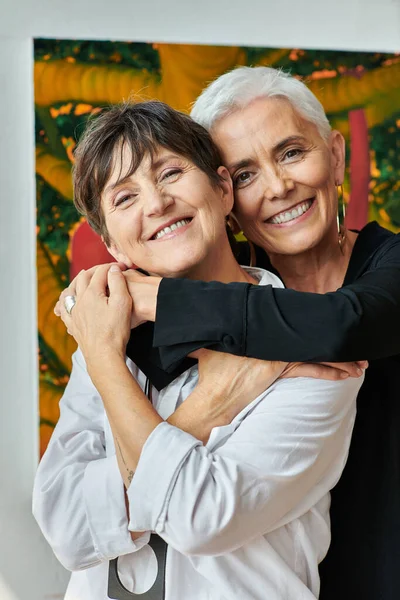 Portrait d'artistes lesbiennes matures heureuses et branchées souriant à la caméra dans un atelier artisanal moderne — Photo de stock