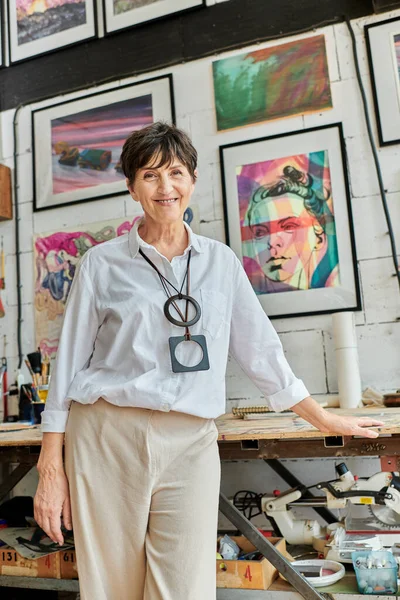 Joyeuse et branchée artiste femme regardant la caméra dans l'atelier d'art avec des peintures expressives colorées — Photo de stock