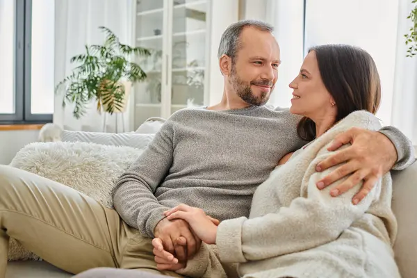 Happy child-free couple holding hands and smiling at each other on couch in living room, serenity — Stock Photo