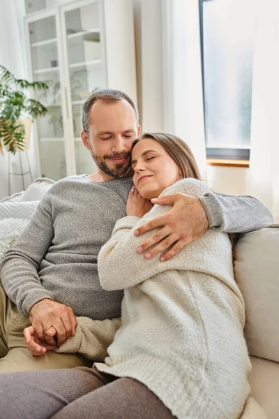 Happy child-free couple with closed eyes embracing on cozy couch in living room, calm lifestyle — Stock Photo