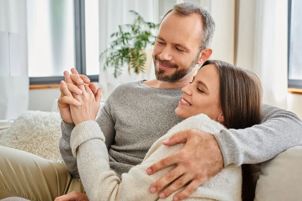 Smiling child-free couple holding hands and embracing on couch in living room, warm relationship — Stock Photo