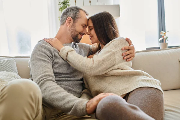 Alegre pareja sin niños sonriendo cara a cara con los ojos cerrados en la sala de estar en casa, serenidad - foto de stock