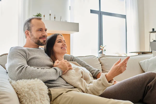 Lächelndes kinderfreies Paar auf bequemer Couch sitzend und im Wohnzimmer wegschauend, entspannen — Stockfoto