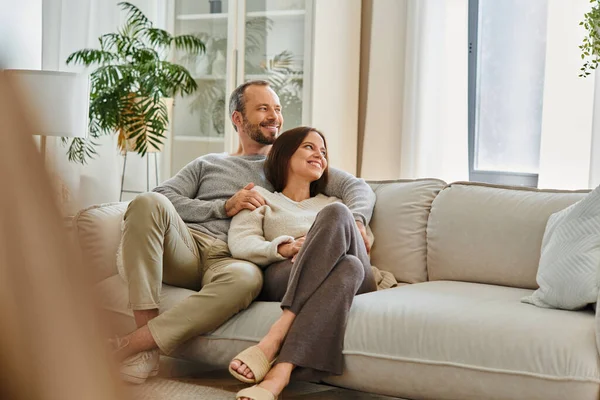 Радостная пара без детей расслабляется на уютном диване в гостиной и смотрит вдаль, досуг в комфорте — стоковое фото