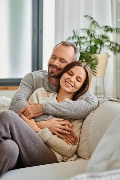 Feliz pareja sin niños abrazando y sonriendo con los ojos cerrados en el sofá en la sala de estar, el amor y la alegría - foto de stock