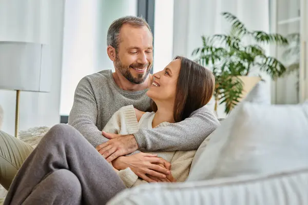 Fröhliches kinderfreies Paar, das sich auf der Couch im Wohnzimmer umarmt und anschaut, Liebe und Freude — Stockfoto