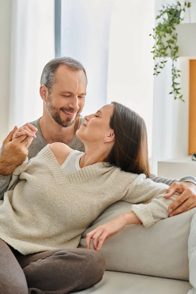 Pleased child-free couple holding hands while sitting on couch in cozy living room, relax and fun — Stock Photo