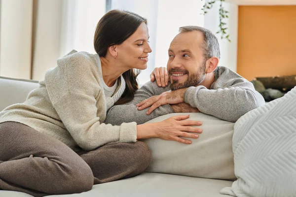 Cheerful child-free couple smiling at each other on cozy couch in living room unity and harmony — Stock Photo
