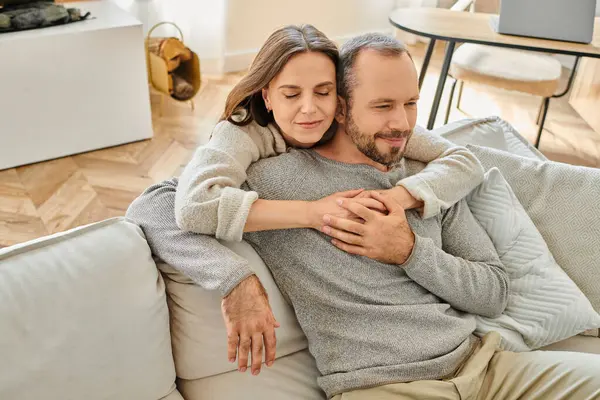 Mujer feliz con los ojos cerrados abrazando al hombre sentado en el sofá en la sala de estar, pareja sin niños - foto de stock