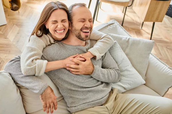 Excited woman with closed eyes embracing husband laughing on couch in living room, child-free couple — Stock Photo