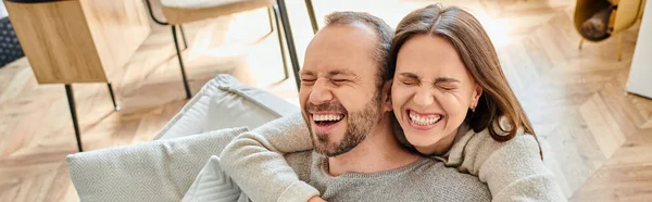 Cheerful woman with closed eyes embracing man laughing on couch at home, child-free couple, banner — Stock Photo