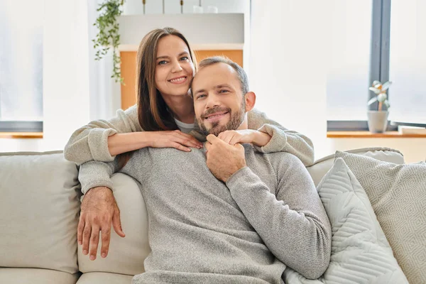 Happy woman hugging smiling husband sitting on couch and looking at camera, child-free lifestyle — Stock Photo
