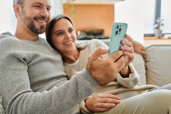 Joyous child-free couple browsing internet on smartphone and relaxing on couch at home, leisure — Stock Photo