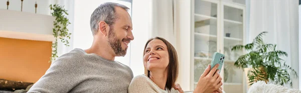 Pleased looking at pleased wife with smartphone at home, child-free lifestyle, horizontal banner — Stock Photo