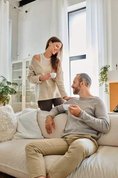Gioiosa coppia senza bambino bere caffè del mattino nel moderno soggiorno di accogliente appartamento, serenità — Foto stock