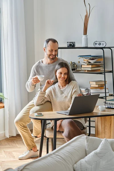 Glückliche Frau arbeitet am Laptop im Homeoffice in der Nähe ihres unterstützenden Ehemannes mit Kaffee, kinderfreies Leben — Stockfoto