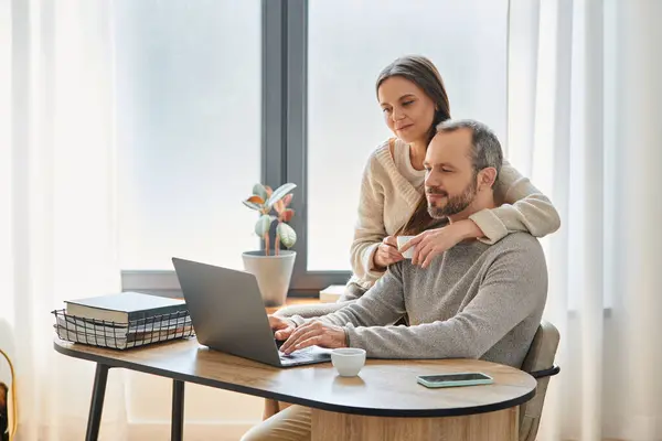 Esposa de apoio com copo de café abraçando marido trabalhando no laptop no escritório em casa, casal sem filhos — Fotografia de Stock