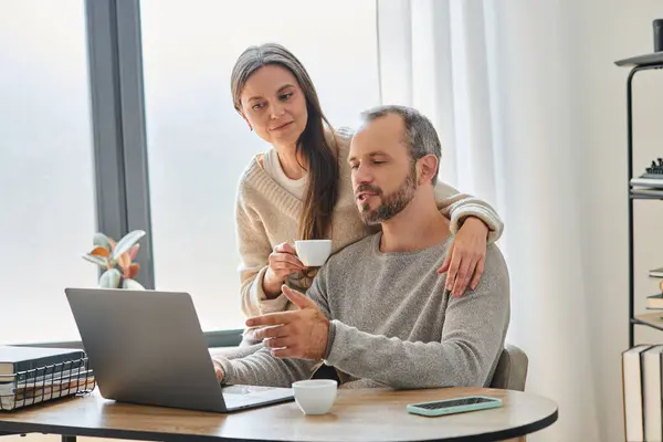 Caring wife with coffee cup supporting husband working on laptop in home office, child-free couple — Stock Photo