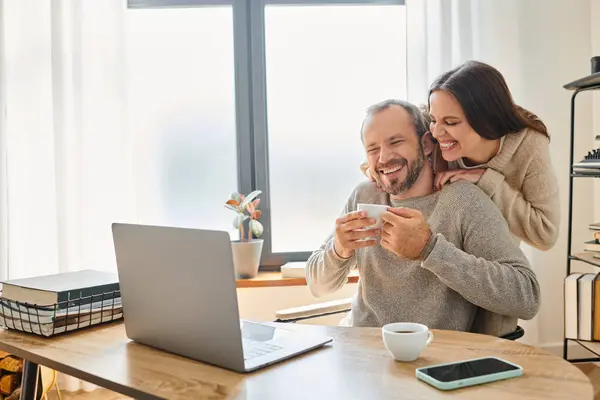 Fröhliche Ehefrau umarmt lächelnden Ehemann sitzt mit Kaffeetasse neben Laptop, kinderfreier Lebensstil — Stockfoto