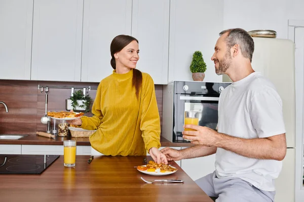 Felice coppia senza figli sorridendo l'un l'altro vicino deliziosa colazione e succo d'arancia fresco — Foto stock