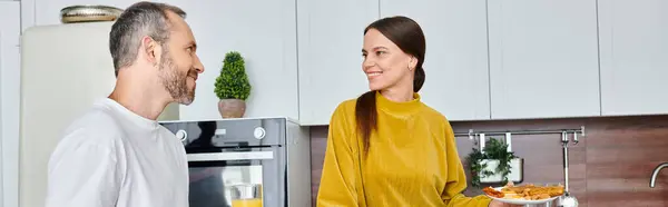 Mulher sorrindo segurando prato com café da manhã caseiro perto de marido feliz na cozinha moderna, banner — Fotografia de Stock