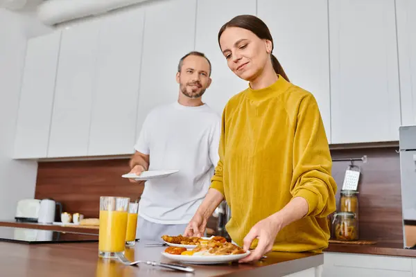 Alegre pareja sin niños que sirve sabroso desayuno en la cocina moderna juntos, serenidad y armonía - foto de stock