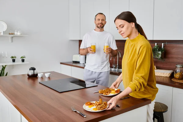 Hombre sosteniendo jugo de naranja cerca de esposa cariñosa que sirve delicioso desayuno en la cocina, vida libre de niños - foto de stock