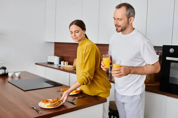 Mann mit Orangensaft neben lächelnder Frau serviert leckeres Frühstück in Küche, kinderfreies Paar — Stockfoto