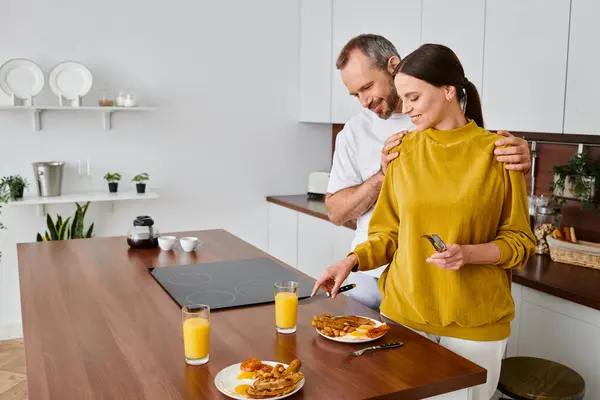 Feliz hombre abrazando hombros de la esposa que sirve sabroso desayuno en la cocina, mañana de pareja libre de niños - foto de stock