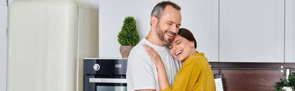 Веселая пара без детей обнимается и улыбается с закрытыми глазами на кухне, горизонтальное знамя — стоковое фото