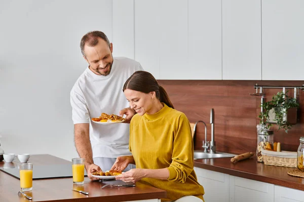 Homme attentionné servant savoureux petit déjeuner fait maison près de sourire dans la cuisine, matin de couple sans enfant — Photo de stock