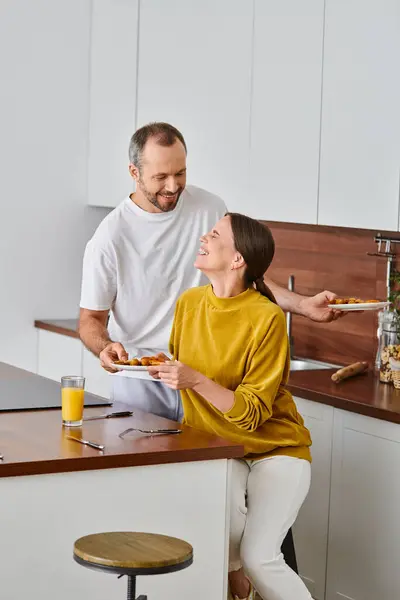 Uomo sorridente che serve gustosa colazione vicino a ridere moglie in cucina, mattina di coppia senza figli — Foto stock