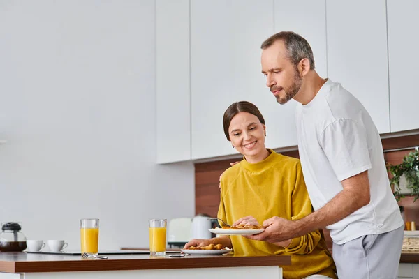 Husband serving delicious breakfast near pleased wife in kitchen, morning of child-free couple — Stock Photo