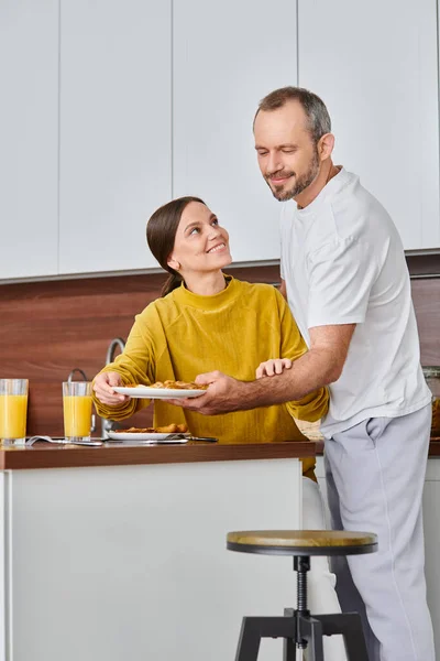 Amazed woman smiling near husband serving delicious breakfast in kitchen, child-free couple — Stock Photo