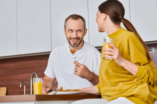 Uomo gioioso avendo deliziosa colazione vicino moglie con succo d'arancia in cucina, stile di vita senza bambini — Foto stock
