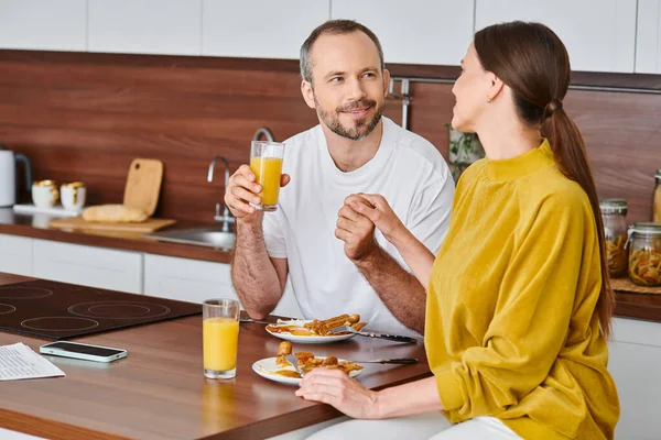 Feliz pareja sin niños tomados de la mano durante el delicioso desayuno en la cocina moderna, serenidad - foto de stock