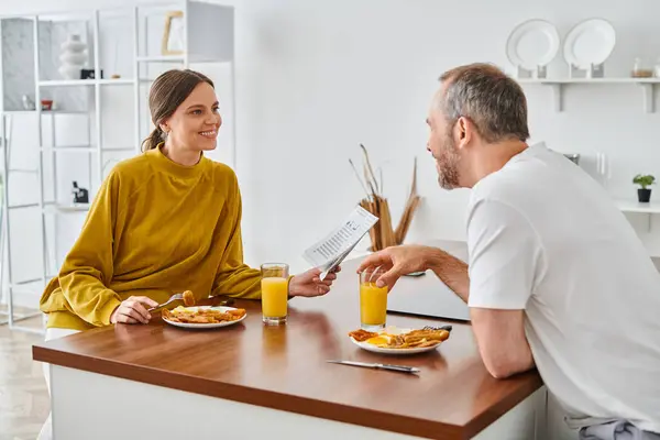 Cheerful woman reading newspaper during breakfast with husband in kitchen, child-free lifestyle — Stock Photo