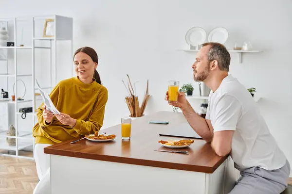 Усміхнена жінка читає новини чоловікові під час сніданку на кухні, вранці бездітна пара — стокове фото