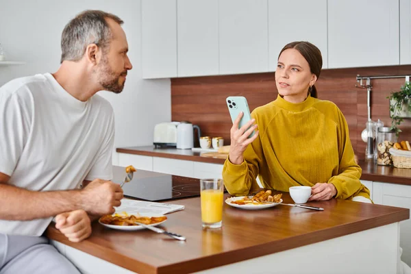 Thoughtful woman holding smartphone near husband during breakfast in kitchen, child-free couple — Stock Photo