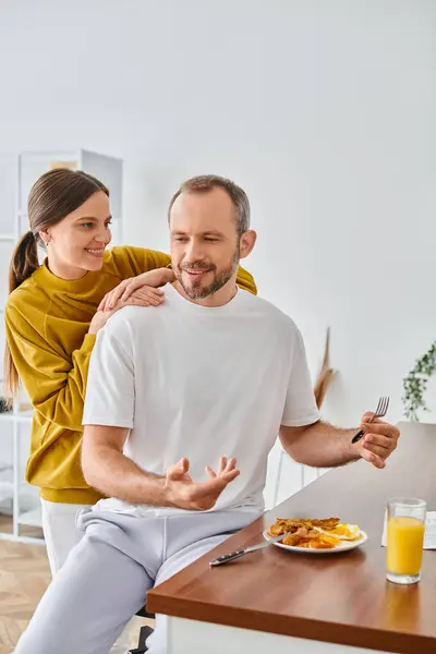 Uomo eccitato che fa colazione e parla con moglie sorridente nella cucina moderna, coppia senza figli — Foto stock