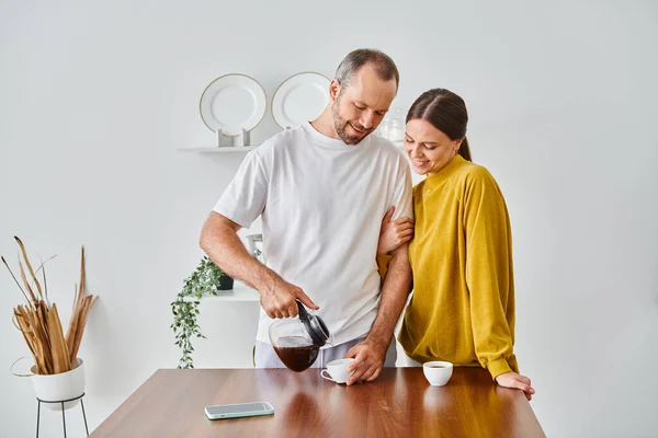 Smiling man pouring fresh aromatic coffee near wife in modern kitchen, morning of child-free couple — Stock Photo
