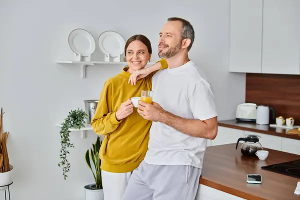 Sonriente pareja sin niños con café aromático y jugo de naranja fresco mirando hacia otro lado en la cocina - foto de stock