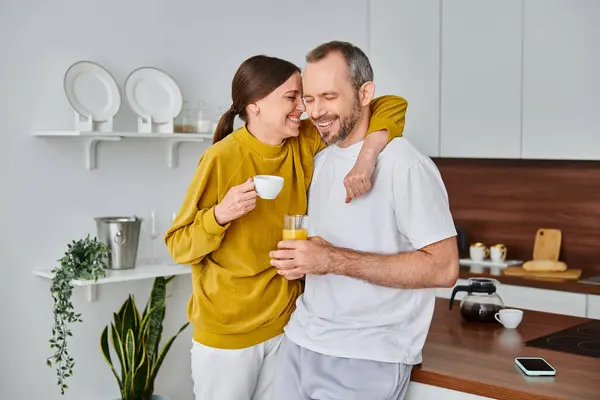 Pareja sin niños encantados con café y zumo de naranja fresco sonriendo con los ojos cerrados en la cocina - foto de stock