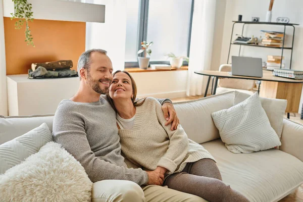 Lächelndes kinderfreies Paar, das sich auf der gemütlichen Couch im modernen Wohnzimmer umarmt, Liebe und Gelassenheit — Stockfoto